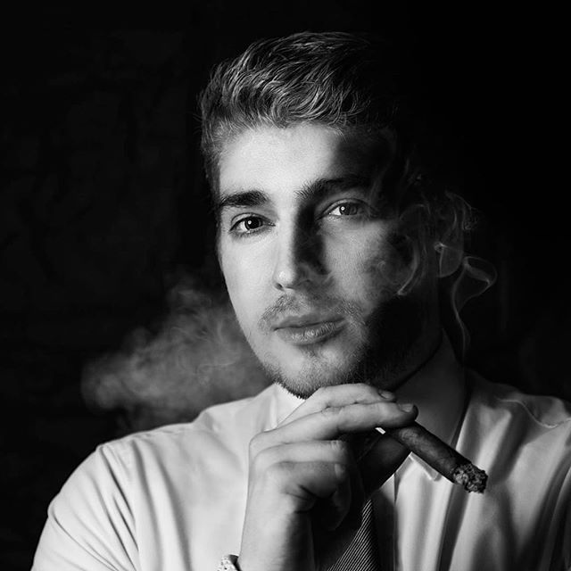 A stylish man in black and white elegantly smokes a cigar in a classic portrait.