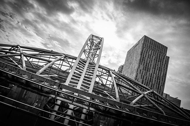 A low-angle monochrome shot of a steel structure in a city, showcasing modern architecture against a dramatic sky.