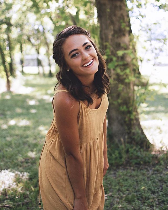 A smiling woman in a yellow dress enjoys a sunny day outdoors.