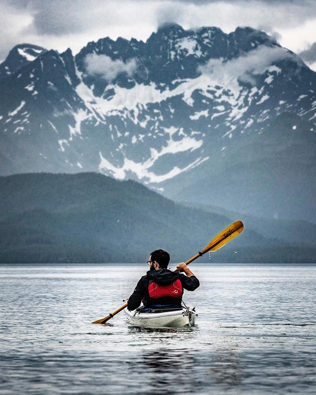 A man kayaks on a calm lake with snow-capped mountains in the background, enjoying a peaceful adventure.