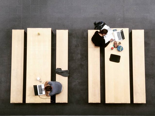 Overhead view of two students studying at tables with laptops in a modern, minimalist study space.