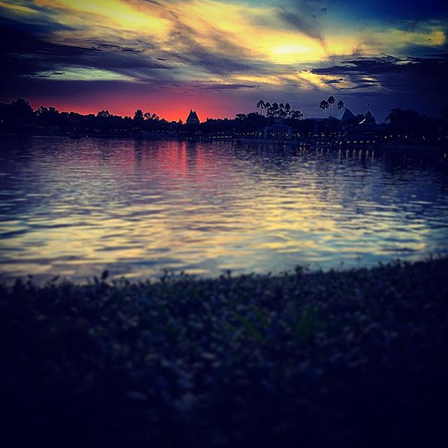 A tranquil lake scene at sunset with silhouetted buildings and a colorful sky reflecting on the water.