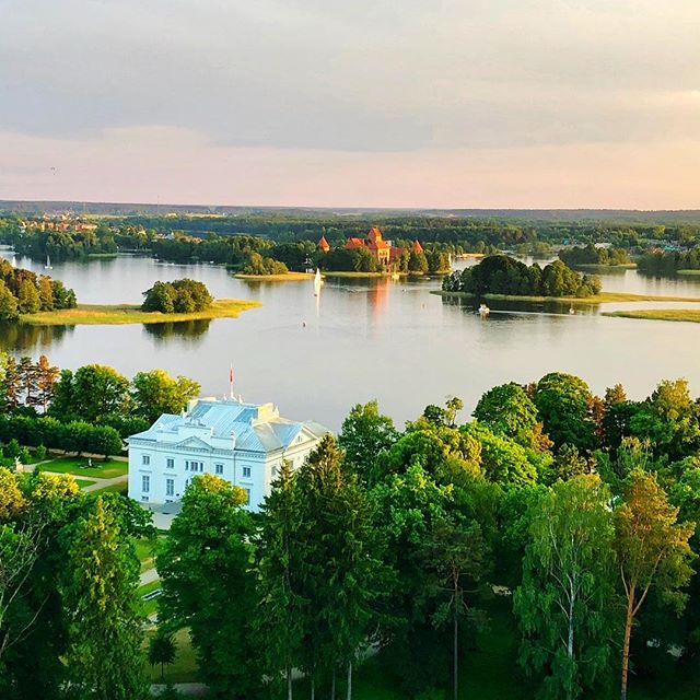 Picturesque view of a castle and white building surrounded by a tranquil lake and lush greenery.