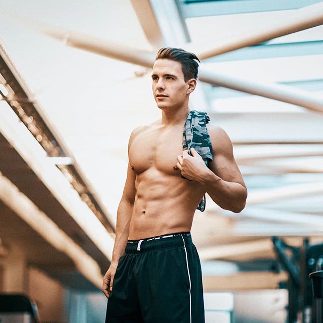 Fit man with a towel stands confidently in a gym, showcasing a healthy lifestyle. 