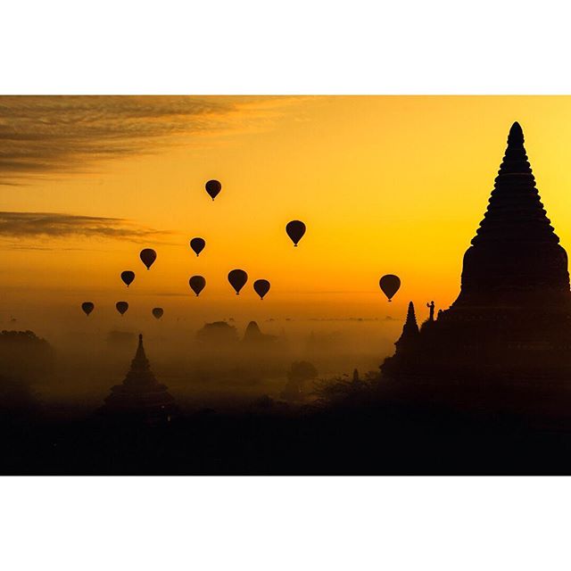 Silhouetted pagodas and hot air balloons float over an ancient skyline at sunrise, creating a serene travel moment.