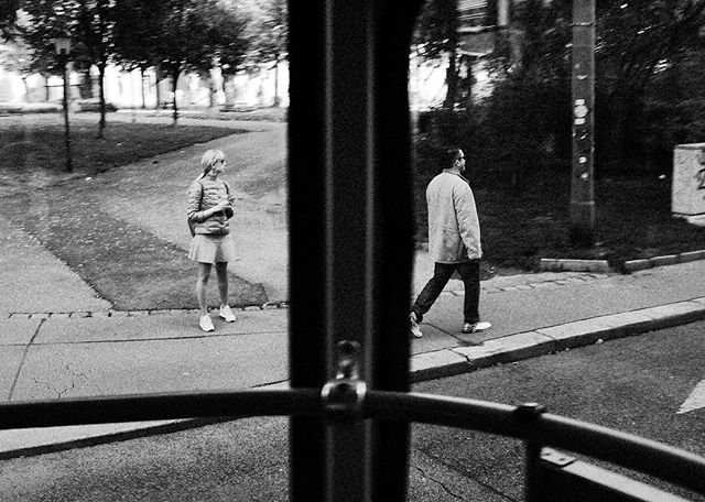 A man and a woman walk on opposite sides of a city street in a black and white photo.