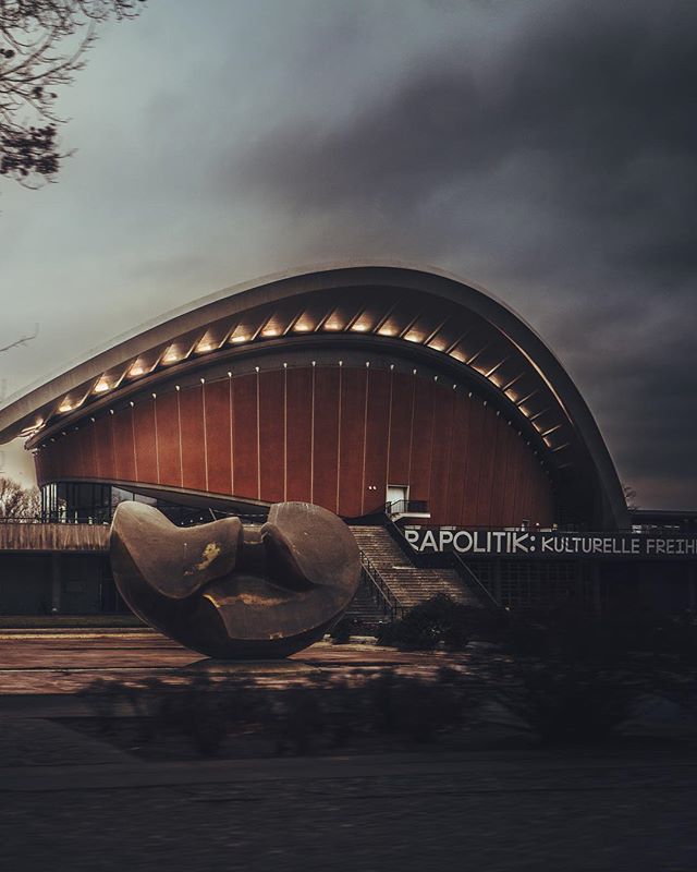 A striking view of Haus der Kulturen der Welt in Berlin, featuring a unique sculpture and modern architecture under a moody sky.