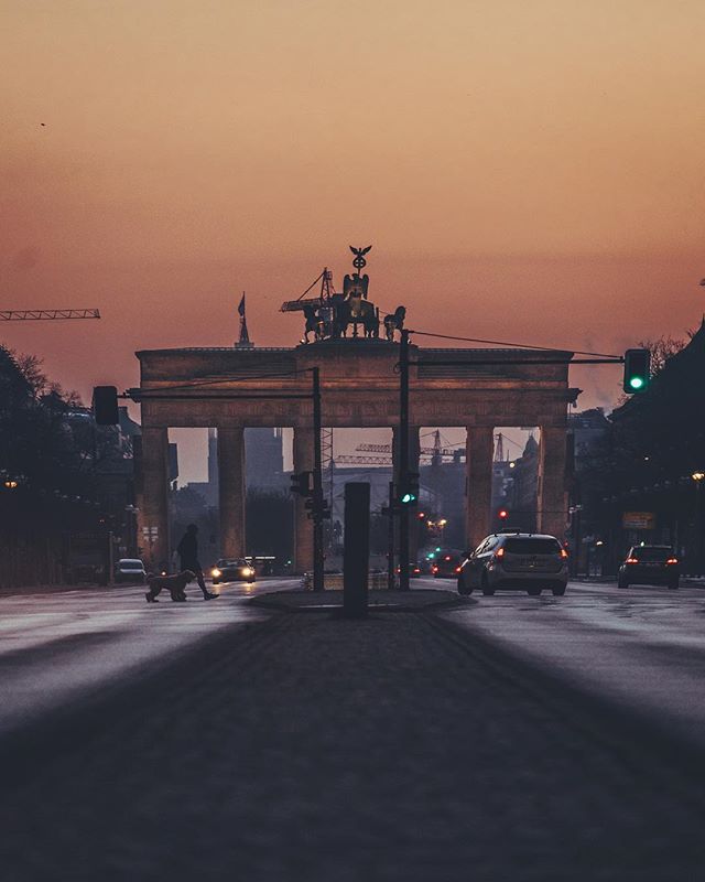 The Brandenburg Gate in Berlin, Germany with a pedestrian crossing the street with a dog at dusk.