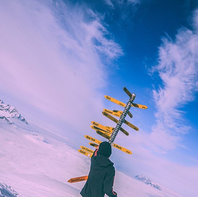 Person standing next to a directional sign at a mountain top with panoramic views. 