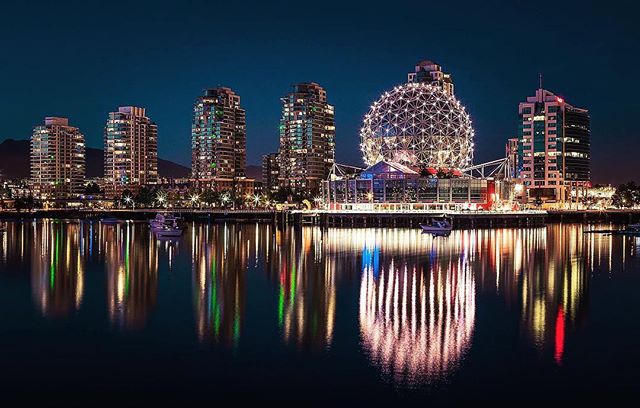 Vancouver's cityscape at night with Science World reflected in the water, showcasing a calm and vibrant urban scene.