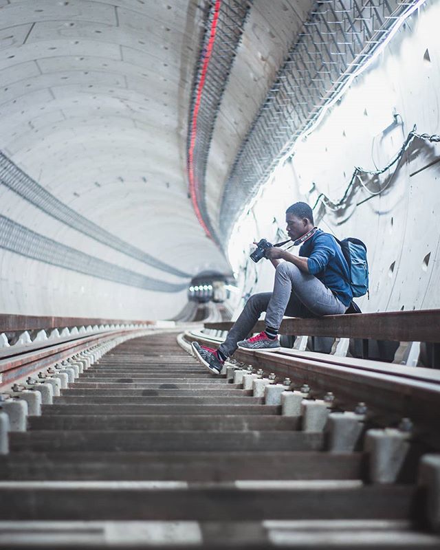A photographer sits on the rail in an empty tunnel, capturing the unique infrastructure and design of the subway system.