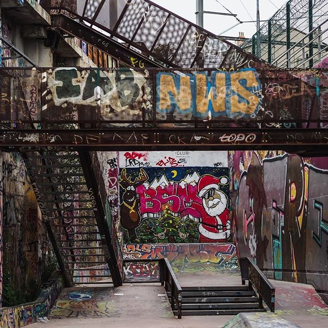 A graffiti-covered skatepark under an urban overpass features vibrant street art and grungy, urban artwork.