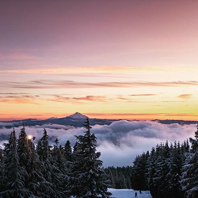 Scenic mountain vista at sunset with snow-covered trees and a skier on the slope.
