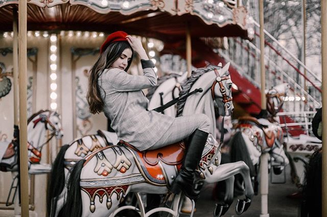 A woman in a red beret enjoys a ride on a decorative carousel horse in a vintage-style setting.