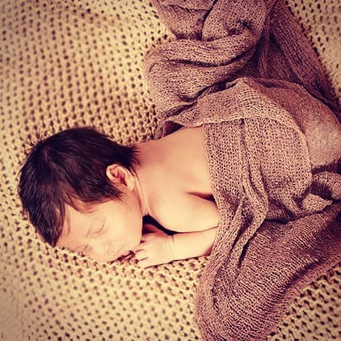 A newborn baby sleeps peacefully, wrapped in a soft blanket. Adorable and serene scene.