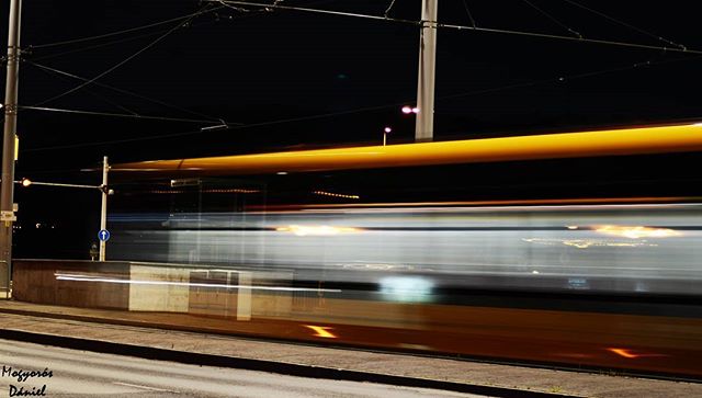 A train speeds through the night, captured in a long exposure with vibrant light trails. A modern view of city transport.