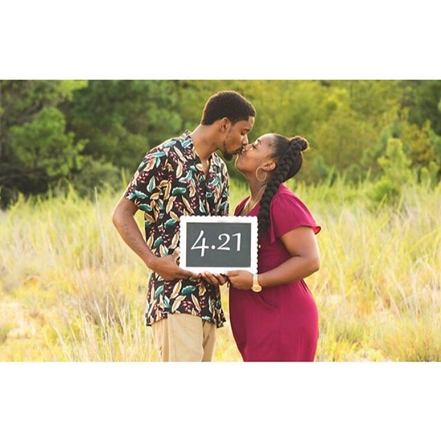 A loving couple kissing in a sunlit field, holding a sign with 4.21.