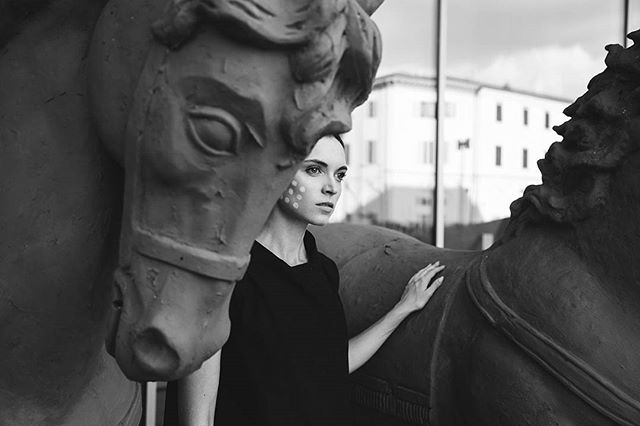 A woman poses with a horse statue, a blend of art and fashion in a monochrome setting.
