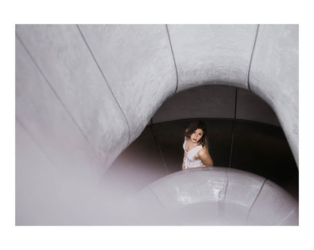 A woman in a white top is seen in a modern architectural tunnel. The image is cool-toned and editorial in style.