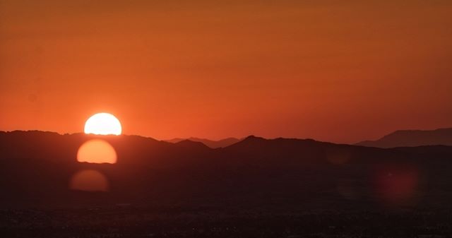 A vibrant orange sunset over mountain silhouettes creates a tranquil landscape scene.