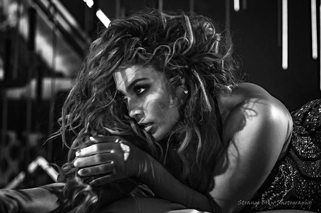 A black and white portrait of a woman with curly hair in a dramatic pose, suitable for fashion or beauty editorials.