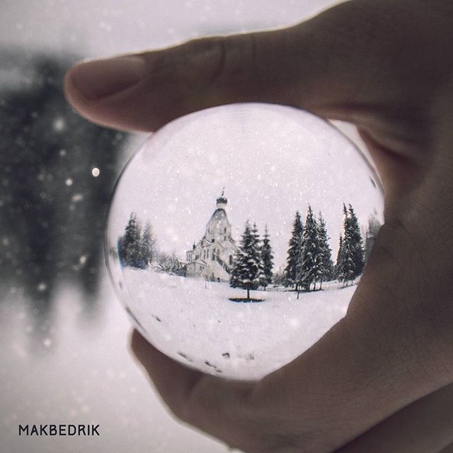 A scenic winter landscape featuring a snow-covered church reflected in a handheld lensball.