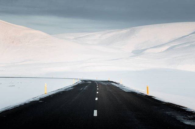 A solitary road cuts through a serene, snow-covered landscape on a moody winter day.