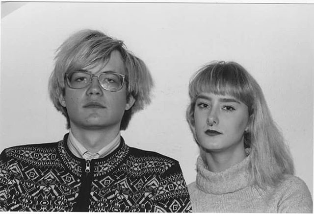 A black and white studio portrait of a man with glasses and a woman wearing a turtleneck.