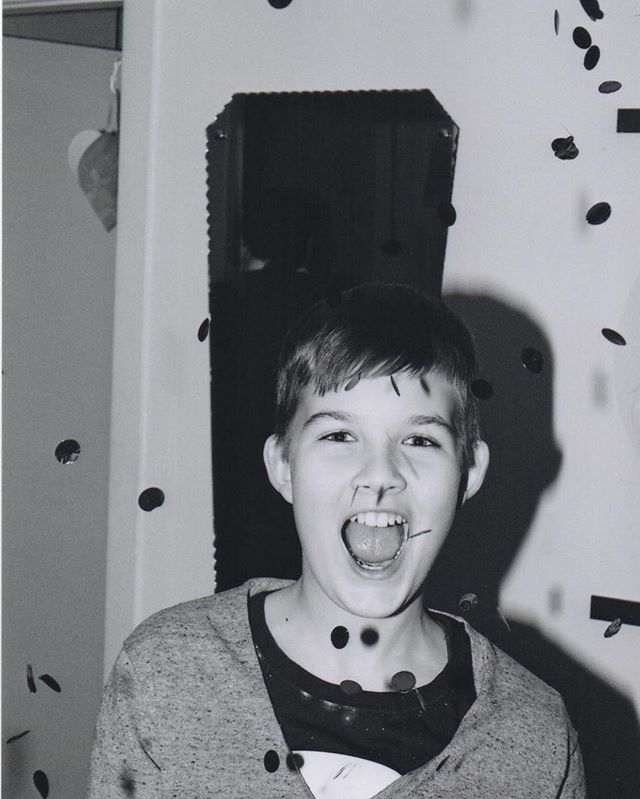 A happy boy celebrates amidst falling confetti at a party, captured in a vintage black and white photo.