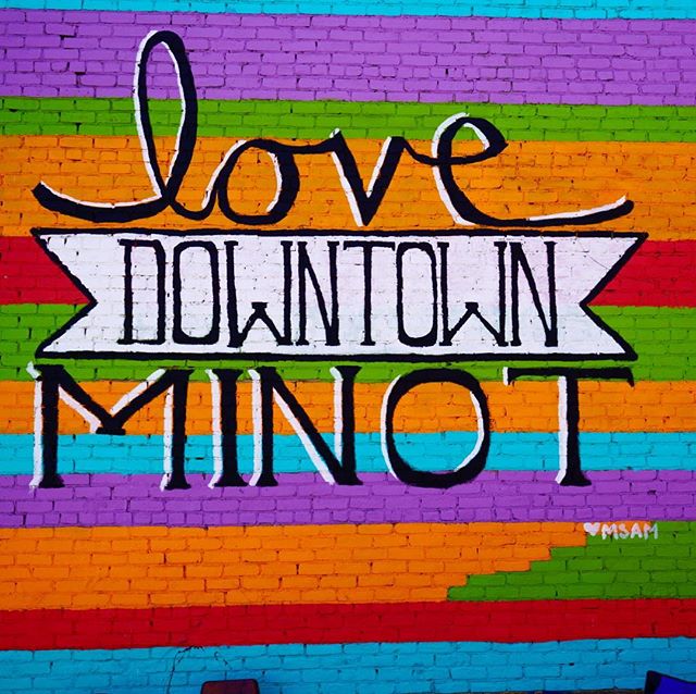 Colorful mural that says 'Love Downtown Minot' painted on a brick wall with horizontal stripes. 