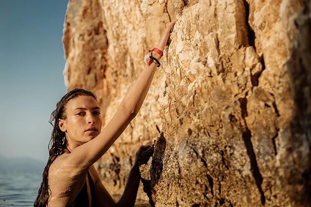 A determined woman rock climbs a coastal cliff face, showcasing strength and adventure in the outdoors.