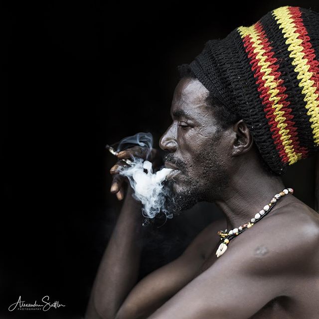 A man with a rasta hat smoking, deep in thought, captured in a close-up with soft, natural lighting for a contemplative mood.