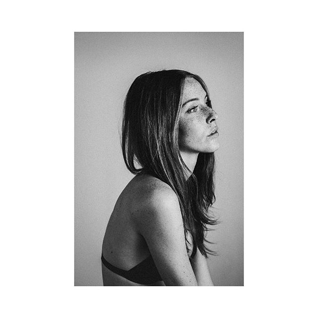 A black and white portrait of a brunette woman with freckles looking serene in a studio.
