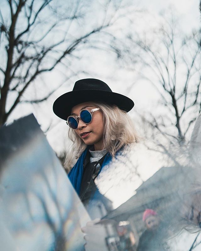 A stylish woman with sunglasses and a hat is captured in an urban outdoor setting with a shallow depth of field.