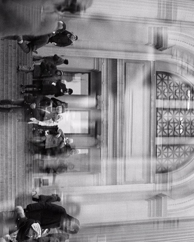 A black and white image captures people walking in a building with blurred motion, creating an artistic vintage feel.