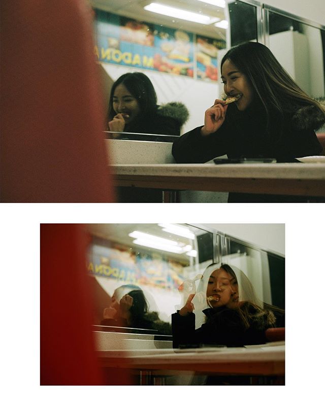 A woman smiles, enjoying a sandwich in a diner, her reflection visible in the vintage-style photo.