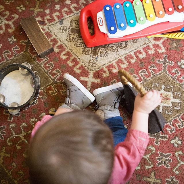A baby is playing with musical toys, including a xylophone and tambourine, on a patterned rug.