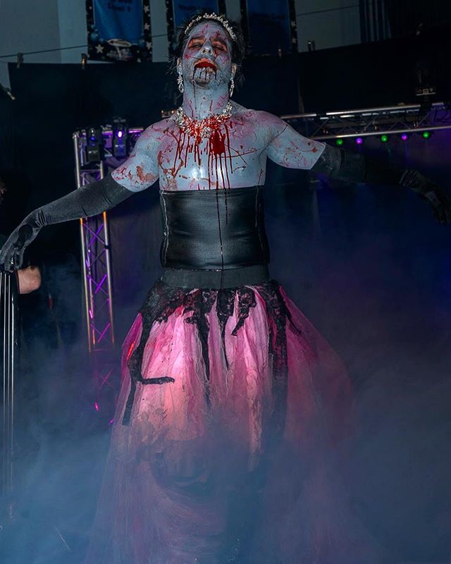 A zombie drag queen performs on stage, covered in gore and wearing a crown.