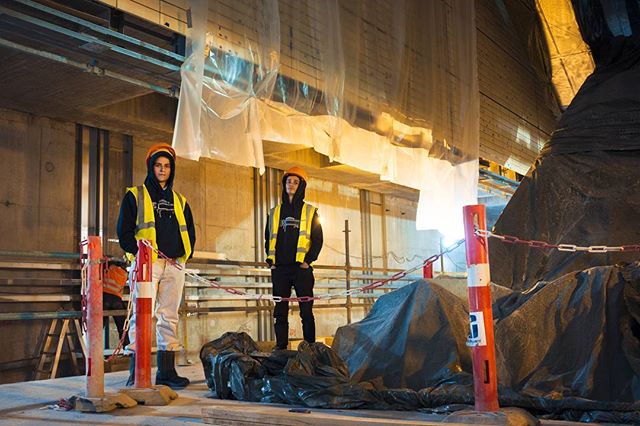 Two construction workers stand in a tunnel, wearing safety vests and hard hats at the construction site.