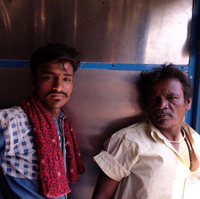 Two men are standing indoors, posing for the camera. They appear relaxed and comfortable in their surroundings.