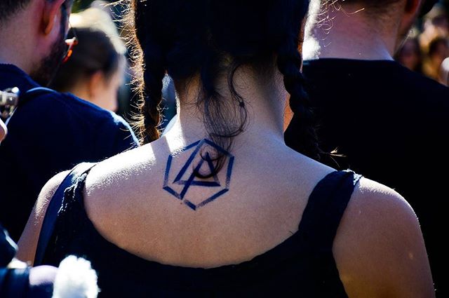 A woman with a Linkin Park tattoo on her neck stands in a crowd.