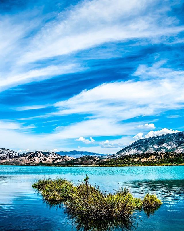 A serene lake surrounded by mountains and lush vegetation under a partly cloudy sky.