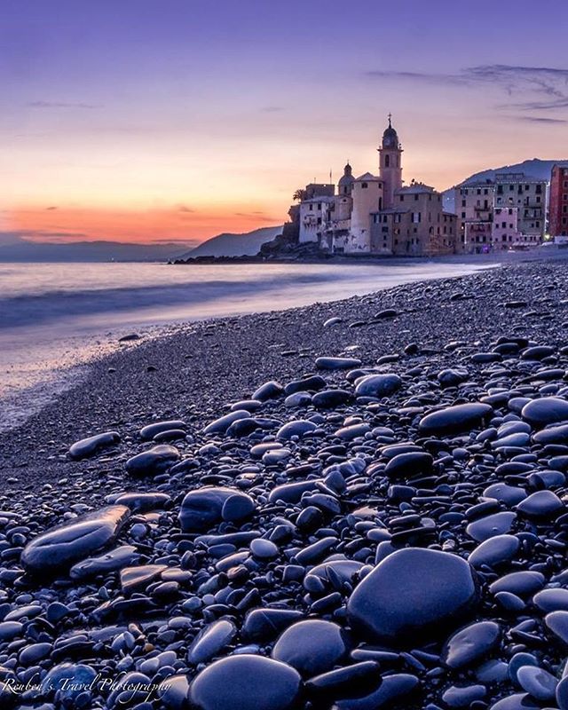 A picturesque coastal town with a beach of rocks under a vibrant sunset sky, creating a serene and inviting travel scene.