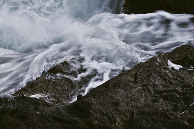 Waves crash against dark rocks in a calming display of nature's power and beauty by the sea.