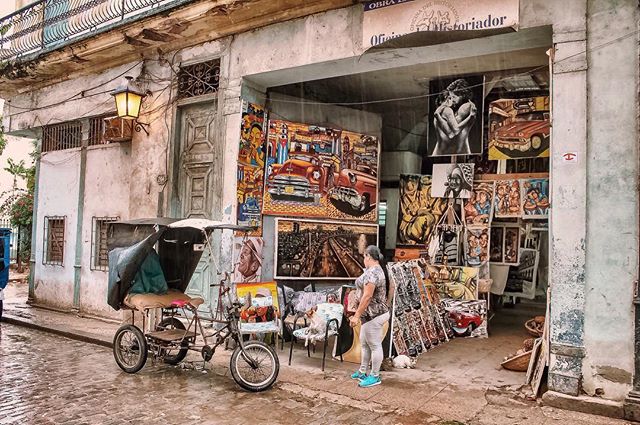 Woman looks at art displayed outside a shop with a tricycle nearby in an urban setting. 