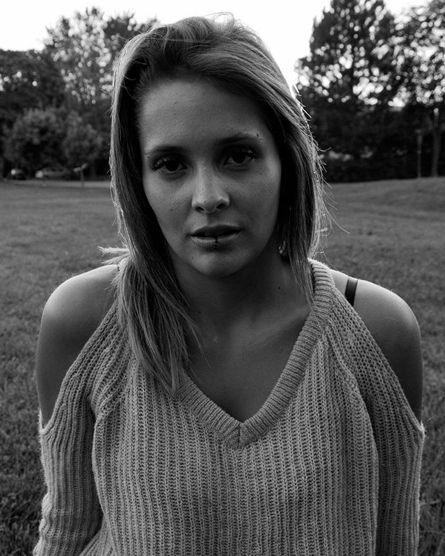 A young woman with a piercing gazes directly at the camera in a black and white outdoor portrait.