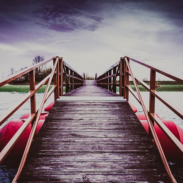 A wooden pontoon bridge stretches over calm water, creating a peaceful and scenic landscape.