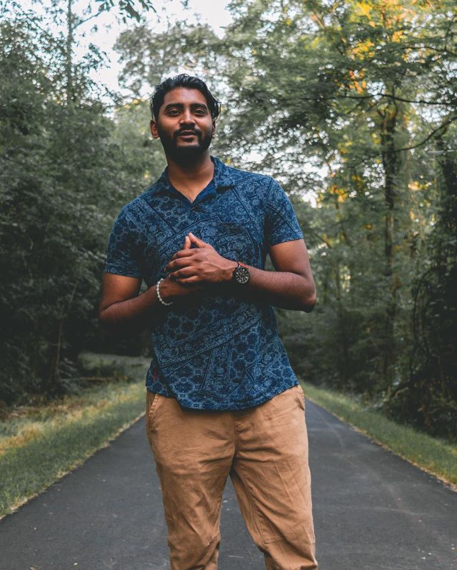 A confident man standing on a road surrounded by trees in a natural outdoor setting.