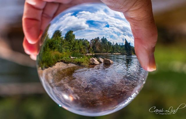 A serene river landscape is captured through a glass sphere, showcasing nature's calm beauty.