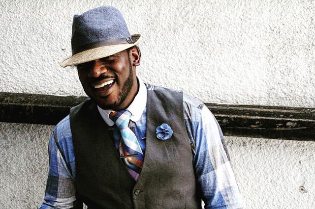 Smiling man in hat, vest and tie against a textured wall. Fashionable, stylish and classic look.